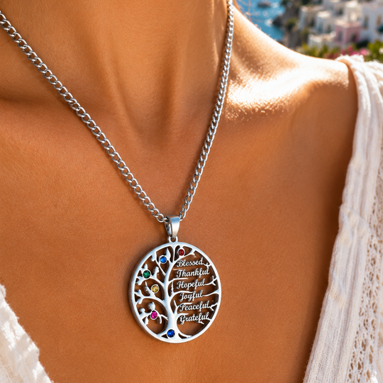 A close-up lifestyle shot of a woman wearing a silver chain necklace with a circular tree-of-life pendant. The pendant features a silver tree silhouette with colorful gemstone accents and engraved script.