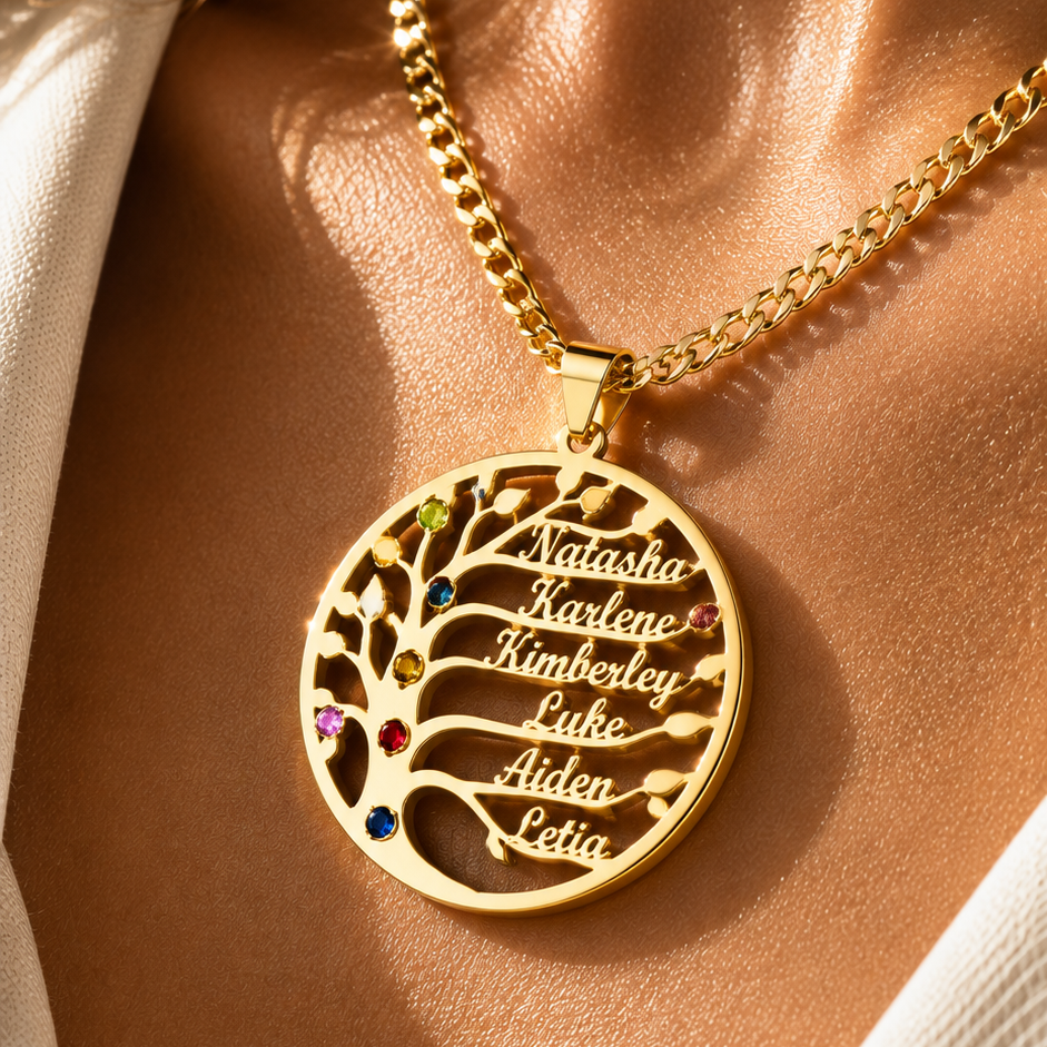 A close-up lifestyle shot of a gold necklace with a circular pendant worn on a model's neck. The pendant features a tree of life design with the names 'Natalia', 'Kimberly', 'Lula', 'Aida', and 'Leda' cut out in the branches, accented with small colorful gemstones.