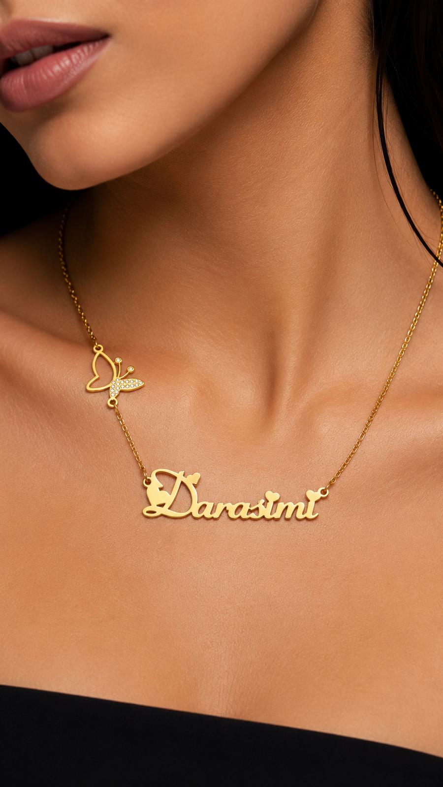 A close-up of a model's neck wearing a gold chain necklace with a butterfly charm and a cursive nameplate reading 'Dara-simt'.