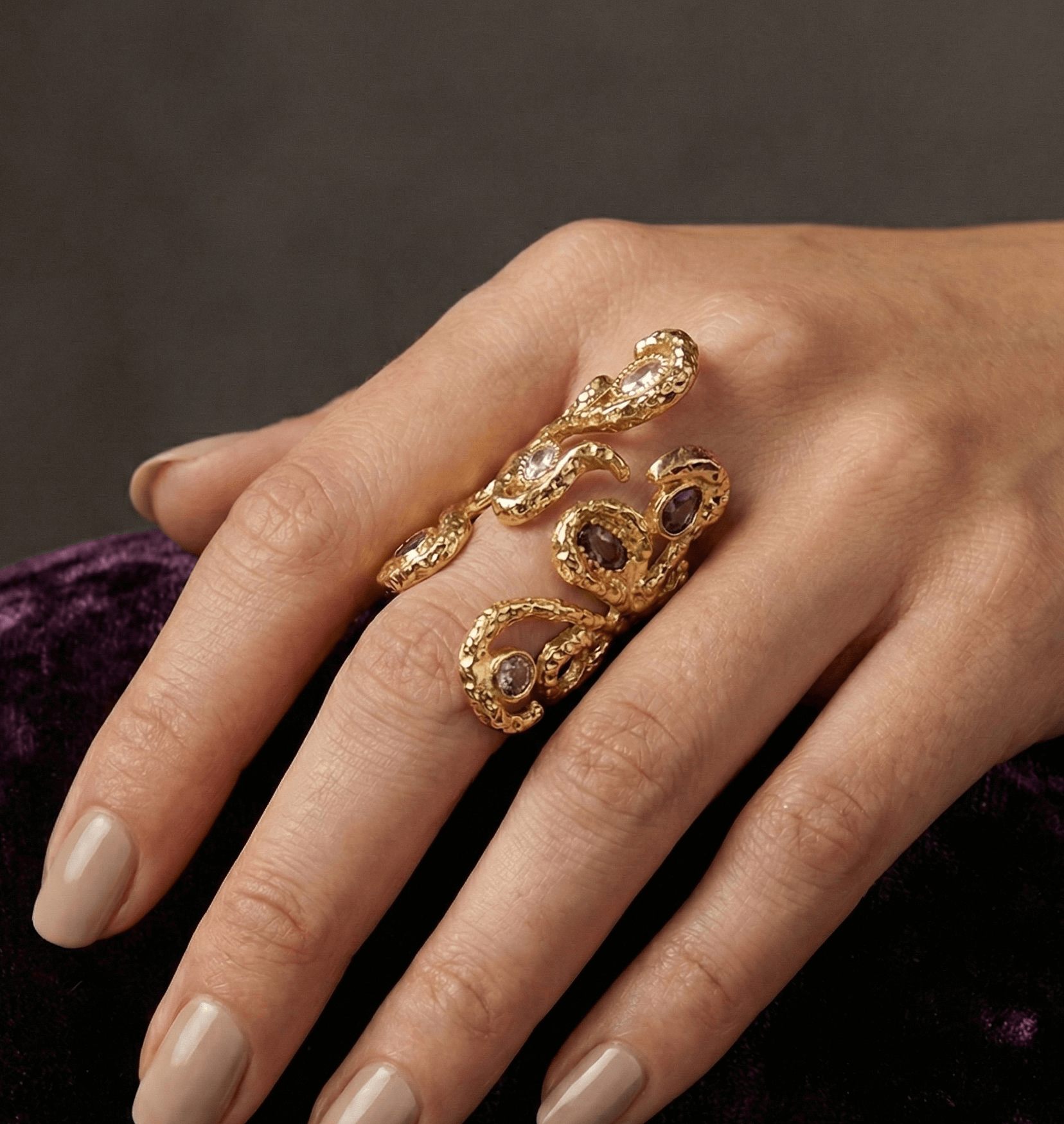 Hand wearing a gold ring with gemstones on a dark background