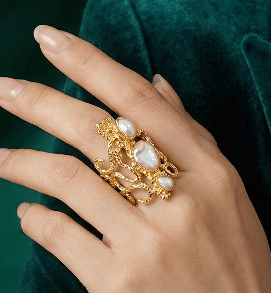 Hand wearing a gold ring with pearls against a green velvet background