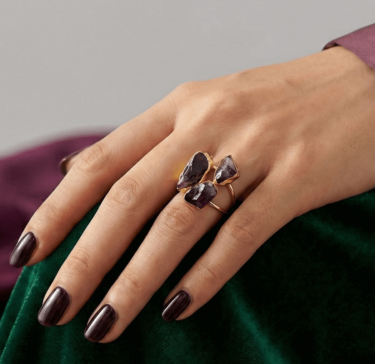 Hand wearing a decorative ring with a purple gemstone on a green fabric background