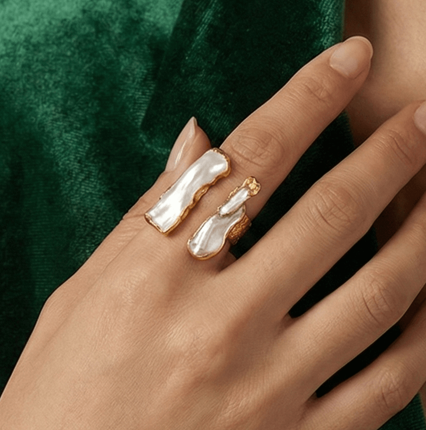 Hand wearing two rings with a green velvet garment in the background