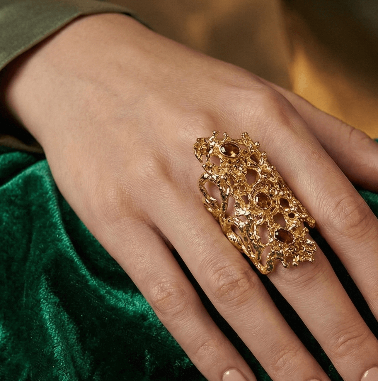 Hand wearing a gold ring with intricate design on a green fabric background