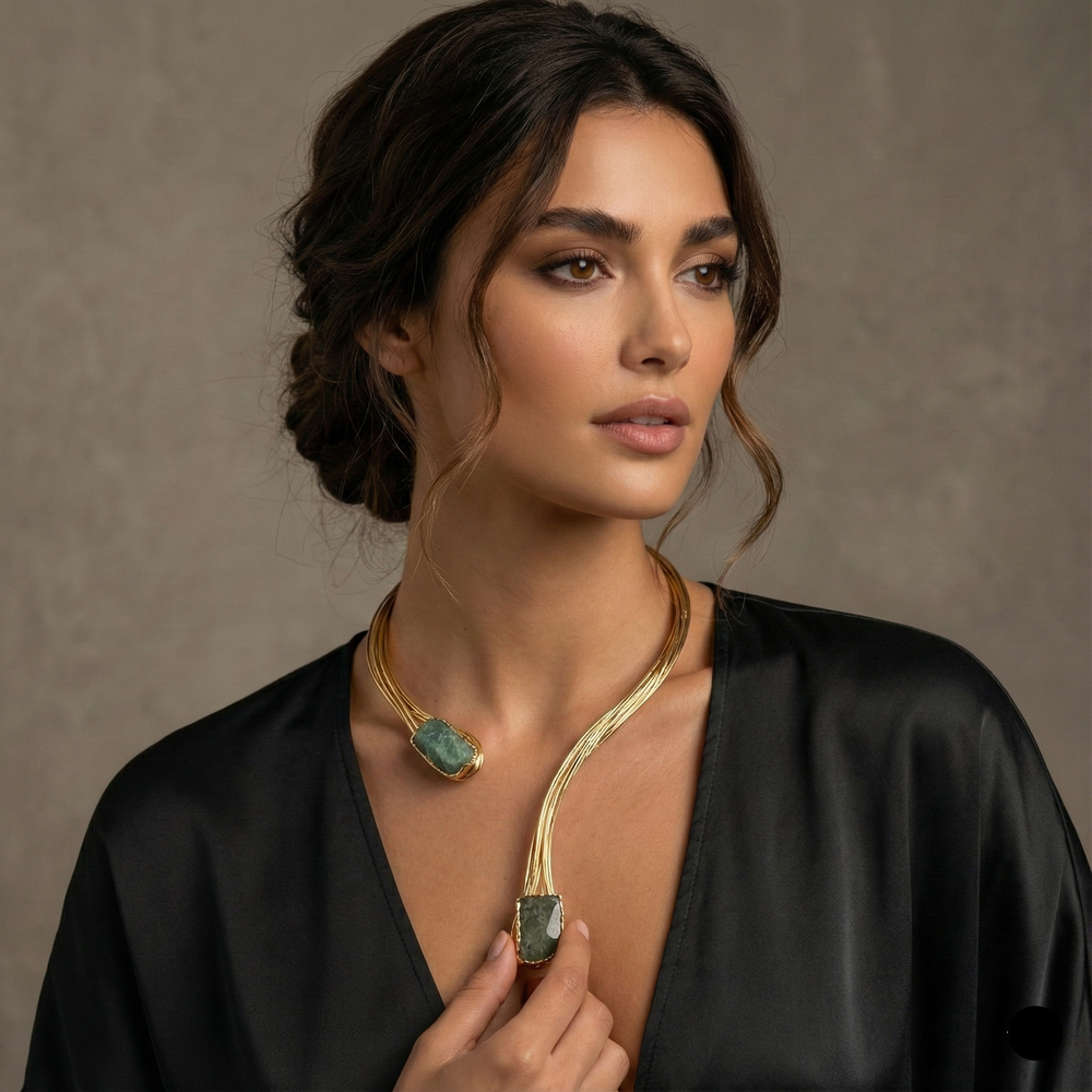Woman wearing a gold necklace with a green pendant against a neutral background